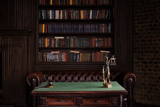 A classic study room with shelves of books, a gavel, and Lady Justice figurine on a green table.